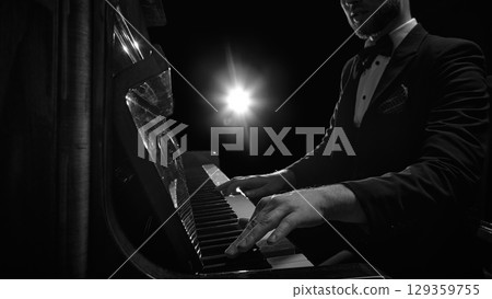 Close-up of male pianist's hands playing piano under dramatic spotlight 129359755