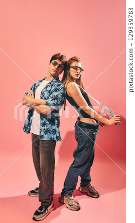 Trendy young man and woman standing back to back in casual streetwear on pink background 129359783