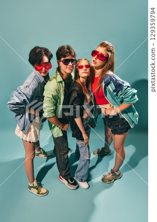 Stylish youth group standing together in colorful retro streetwear and sunglasses against turquoise background 129359794