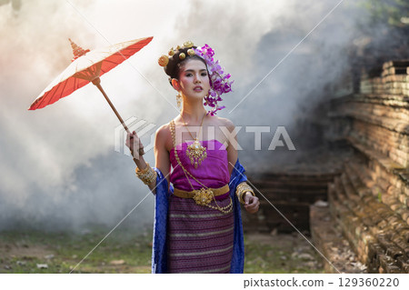 Beautiful Thai woman wearing thai traditional clothing with red umbrella in amid the smoke and fog. 129360220