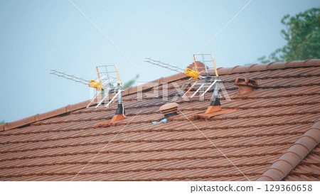 Two television antennas mounted on a tiled rooftop during light rain, France Two television antennas mounted on a tiled rooftop during light rain, France 129360658