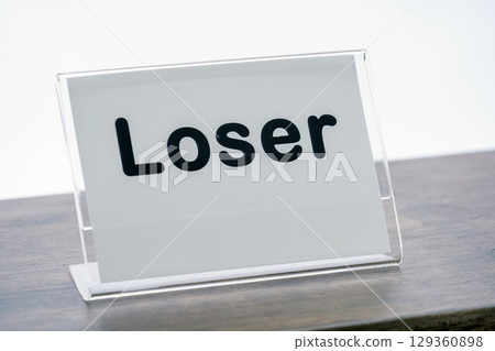 Sign with word Loser is displayed on wooden counter, conveying humorous or sarcastic message. sign is encased in clear plastic holder, emphasizing its playful nature Sign with word Loser is displayed on wooden counter, conveying humorous or sarcastic message. sign is encased in clear plastic holder, emphasizing its playful nature 129360898