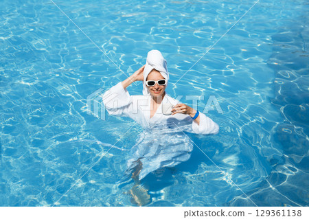 A girl in a white coat swims in a blue pool. Wearing sunglasses and a towel. Epilation of legs, varicose veins. Rest, relaxation on the beach, at the hotel. A woman in freedom. Vacation. High quality A girl in a white coat swims in a blue pool. Wearing sunglasses and a towel. Epilation of legs, varicose veins. Rest, relaxation on the beach, at the hotel. A woman in freedom. Vacation. High quality 129361138