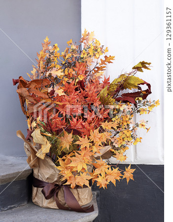 Vibrant autumn arrangement with colorful foliage placed by a minimalist wall Vibrant autumn arrangement with colorful foliage placed by a minimalist wall 129361157