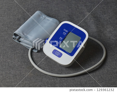 Digital blood pressure monitor and cuff laid out on a textured gray background. High quality photo Digital blood pressure monitor and cuff laid out on a textured gray background. High quality photo 129361232