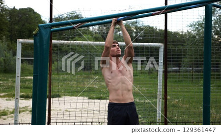 Young muscular sportsman doing pull ups at sports ground. Athletic guy exercising outdoor. Strong sporty man working out at summer nature. Concept of healthy and active lifestyle. Slow motion Young muscular sportsman doing pull ups at sports ground. Athletic guy exercising outdoor. Strong sporty man working out at summer nature. Concept of healthy and active lifestyle. Slow motion 129361447
