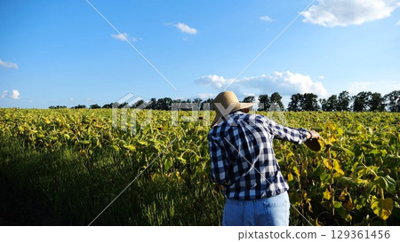 Female agronomist exploring plants at yellow meadow. Adult farmer examining ripe sunflowers at field on sunny day. Beautiful scenic landscape. Concept of agriculture and agronomy business. Close up Female agronomist exploring plants at yellow meadow. Adult farmer examining ripe sunflowers at field on sunny day. Beautiful scenic landscape. Concept of agriculture and agronomy business. Close up 129361456