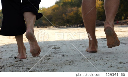 Male and female legs of pair walking on sandy beach. Bare feet of couple stepping along sand shore at sunny day. Lovers spending time together at resort. Concept of summer vacation or holiday Male and female legs of pair walking on sandy beach. Bare feet of couple stepping along sand shore at sunny day. Lovers spending time together at resort. Concept of summer vacation or holiday 129361460