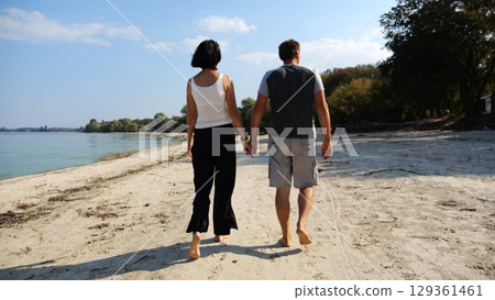 Romantic couple holding hands of each other and walking at coastline. Happy pair going along seashore at sunny day. Lovers spending time together at resort. Concept of vacation or holiday. Slow motion 129361461