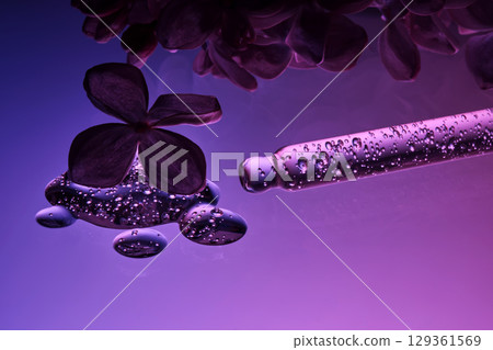 Cosmetic pipette with serum and lilac flowers on a purple background. Cosmetic pipette with serum and lilac flowers on a purple background. 129361569