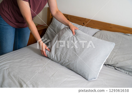 Woman holding a pillow with fresh clean pillowcases, grey cotton bed sheets Woman holding a pillow with fresh clean pillowcases, grey cotton bed sheets 129361638