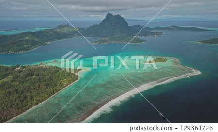 Aerial panorama vibrant coral reef in crystal clear, shallow water of Bora Bora turquoise lagoon, framed by majestic green mountain Otemanu rising dramatically in background. Exotic travel getaway. Aerial panorama vibrant coral reef in crystal clear, shallow water of Bora Bora turquoise lagoon, framed by majestic green mountain Otemanu rising dramatically in background. Exotic travel getaway. 129361726
