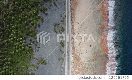 French Polynesia, Rangiroa island: Aerial view capturing a thin road separating lush greenpalm trees vegetation from sandy beach and crashing ocean waves. Drone flight top down French Polynesia, Rangiroa island: Aerial view capturing a thin road separating lush greenpalm trees vegetation from sandy beach and crashing ocean waves. Drone flight top down 129361735