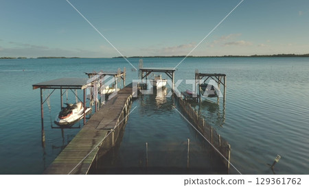 Wooden pier extending into turquoise lagoon, revealing shallow seabed, moored boats, and distant horizon under sunny skies, capturing tropical paradise landscape Wooden pier extending into turquoise lagoon, revealing shallow seabed, moored boats, and distant horizon under sunny skies, capturing tropical paradise landscape 129361762