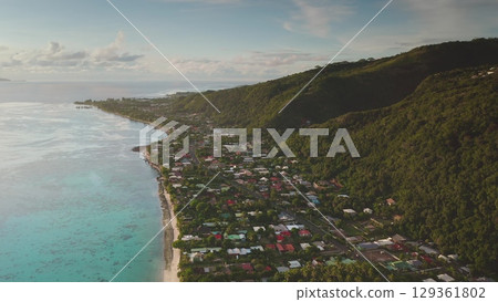 Aerial drone revealing Tahiti's vibrant coastline, where colorful houses blend with lush volcanic slopes, illuminated by the warm glow of sunset Aerial drone revealing Tahiti's vibrant coastline, where colorful houses blend with lush volcanic slopes, illuminated by the warm glow of sunset 129361802