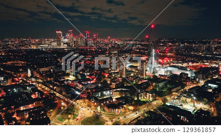 Breathtaking aerial view of London at night, highlighting the vibrant glow of Canary Wharf amidst a bustling urban landscape filled with illuminated buildings and dynamic energy. Drone flight 129361857