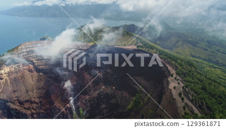 Rising white smoke and gas from a volcano crater on Flores Island, Indonesia, with Ende city visible in the background, captured by a high-flying drone 129361871