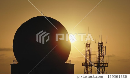 Malta: Silhouette of large radome and radio towers against a warm orange sunset sky in Malta, evoking a military or spy base atmosphere. Drone flight Malta: Silhouette of large radome and radio towers against a warm orange sunset sky in Malta, evoking a military or spy base atmosphere. Drone flight 129361886