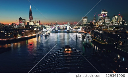 Illuminated London city skyline at sunset, Tower Bridge, The Shard, and a ferry navigating the River Thames. Night lights cityscape. United Kingdom, Europe. Travel destination. Drone flight Illuminated London city skyline at sunset, Tower Bridge, The Shard, and a ferry navigating the River Thames. Night lights cityscape. United Kingdom, Europe. Travel destination. Drone flight 129361908