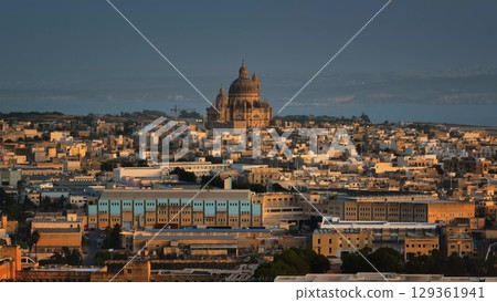 Malta, Comino island: Gozo Cathedral Church of Saint John the Baptist, Rotunda of Xewkija rising over Victoria warm toned cityscape, in golden sunset light, picturesque view of urban landscape 129361941