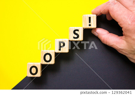 Oops symbol. Concept word Oops on beautiful wooden blocks. Beautiful yellow and black background. Businessman hand. Business lifestyle oops concept. Copy space. Oops symbol. Concept word Oops on beautiful wooden blocks. Beautiful yellow and black background. Businessman hand. Business lifestyle oops concept. Copy space. 129362041