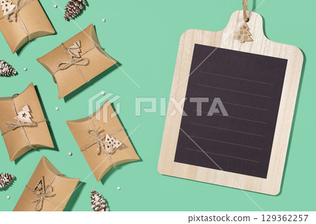 Christmas eco friendly composition. Craft gift boxes with decoration and chalk board with place for text on a green background. Christmas, winter holiday, new year concept. Flat lay, copy space Christmas eco friendly composition. Craft gift boxes with decoration and chalk board with place for text on a green background. Christmas, winter holiday, new year concept. Flat lay, copy space 129362257