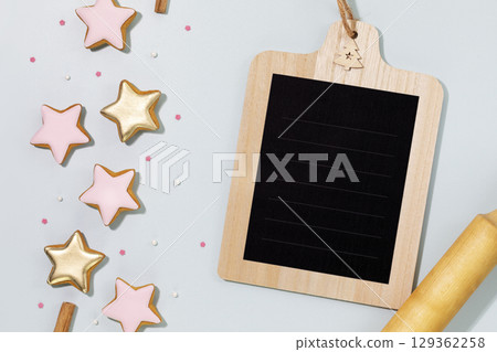 Cooking holiday cookies. Food holiday composition with ginger cookies in the form of stars, covered with glaze with a dough gurney and a chalk bord with place to write a recipe or ingredients 129362258