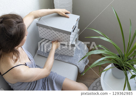 Woman sitting in the couch in cozy room, assembling carton box. Indoors 129362985