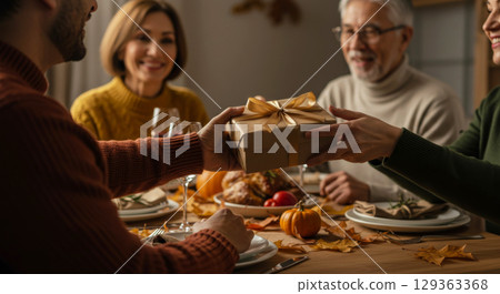 Family giving a gift at a Thanksgiving dinner table with turkey and autumn decor. 129363368