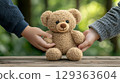 Tender hands holding light brown teddy bear outdoors 129363604