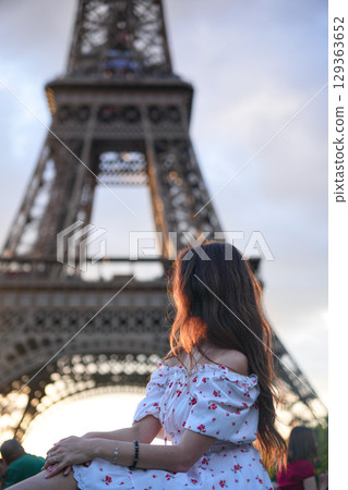 Woman in white floral dress sitting near Eiffel Tower in Paris at sunset Woman in white floral dress sitting near Eiffel Tower in Paris at sunset 129363652
