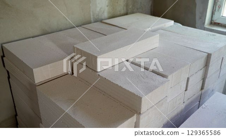 Stack of aerated concrete blocks awaiting use in construction. White aerated concrete blocks stacked neatly, ready for use in a building project, signifying preparation and the start of construction. Stack of aerated concrete blocks awaiting use in construction. White aerated concrete blocks stacked neatly, ready for use in a building project, signifying preparation and the start of construction. 129365586