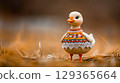 Goose figurine, adorned with embroidered dress and lace trim, stands amidst bed of golden hay 129365664