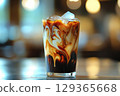 Refreshing iced coffee drink swirling with milk and topped with ice cubes, served in glass on table 129365668