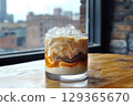Iced coffee drink with creamy milk and ice swirling in rocks glass on wooden table beside window 129365670