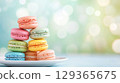 Pyramid of colorful macarons sits on white plate on pastel toned backdrop, copy space 129365675
