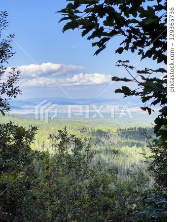 Landscape in the foothills of the Tatras. Mountain peaks against the blue sky and clouds are visible through branches of the trees. 129365736