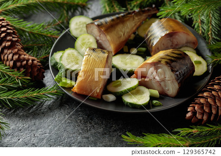 Smoked mackerel with fresh cucumber and green onions on a black plate. 129365742