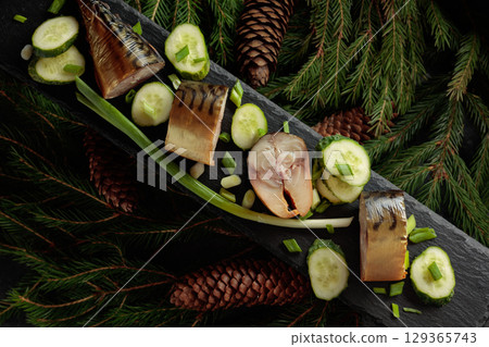 Smoked mackerel with fresh cucumber and green onions on a black plate. 129365743