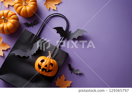 Halloween black gift bag with pumpkin and flying bats surrounded by fall leaves on purple background 129365797