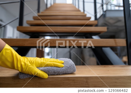 Professional cleaner wearing gloves sanitizing wooden stairway with microfiber cloth 129366482