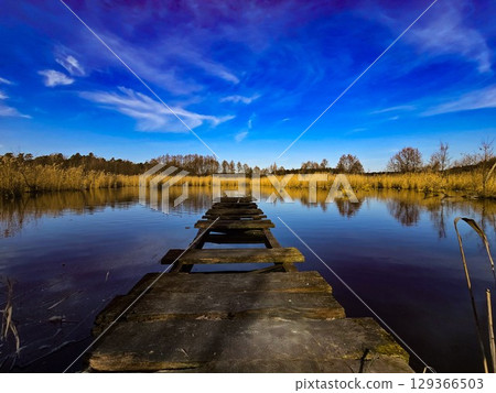 Old Wooden Pier on Calm Lake Under Vibrant Blue Sky 129366503
