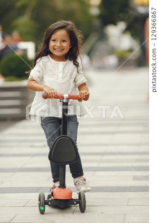 Child on kick scooter in park. Kids learn to skate roller board. Little girl skating on sunny summer day. 129366867