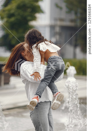 Family near the city fountain. Mother with gaughter playing with water. 129366884