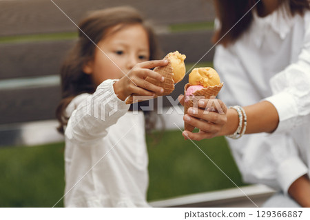 Family in a city. Little girl eats ice cream. Mother with daughter sitting on a bench. 129366887