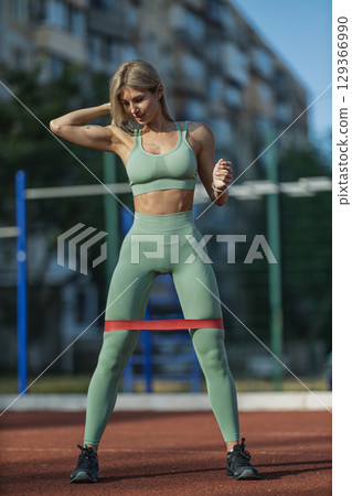 sporty girl wearing a green athletic outfit performs resistance band exercises at an outdoor gym 129366990