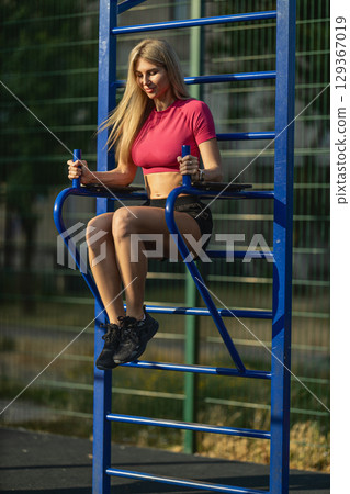 fit woman performs a workout on blue exercise bars in a park setting, showcasing her strength and determination under the sun The atmosphere is active and encouraging fit woman performs a workout on blue exercise bars in a park setting, showcasing her strength and determination under the sun The atmosphere is active and encouraging 129367019