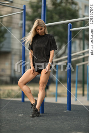 fit woman engages in a workout session in a sports park, dressed in black athletic wear She stands confidently near blue bars, showcasing her strength and determination under natural lighting fit woman engages in a workout session in a sports park, dressed in black athletic wear She stands confidently near blue bars, showcasing her strength and determination under natural lighting 129367048