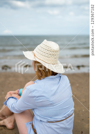 Woman seen from back, on the sandy beach. Cloudy day. 129367182