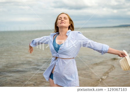 Happy woman at the seaside, enjoying her vacation. Cloudy day. Happy woman at the seaside, enjoying her vacation. Cloudy day. 129367183
